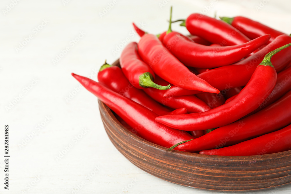 Wooden bowl with red hot chili peppers on white table, closeup. Space for text