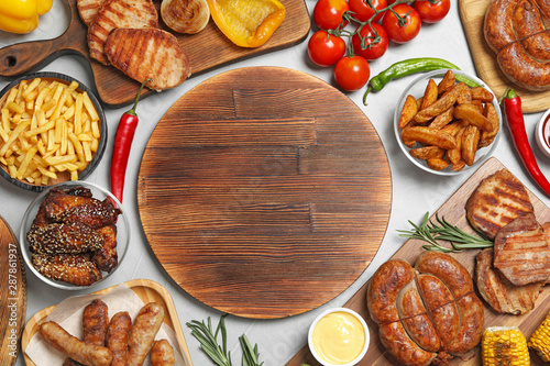 Flat lay composition with barbecued meat and vegetables on white wooden table. Space for text