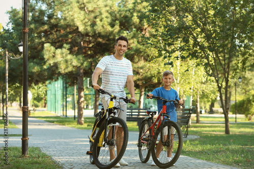 Dad and son riding bicycles in park on sunny day