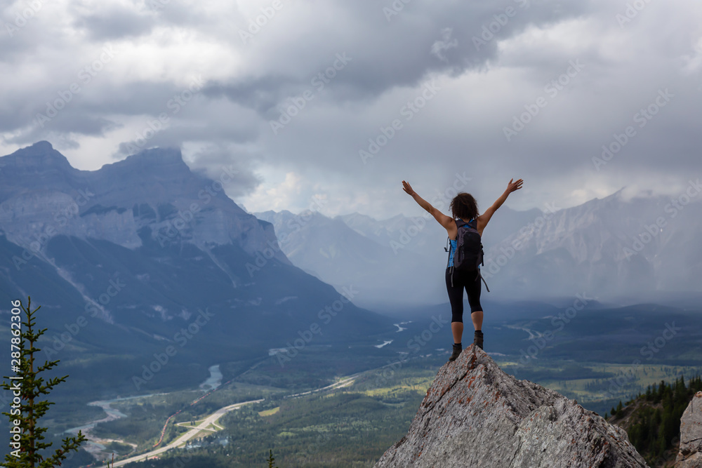 Adventurous Caucasian Girl with open arms is on top of rocky mountain during a cloudy and rainy day. Taken from Mt Lady MacDonald, Canmore, Alberta, Canada. Adventurous Caucasian Girl with open arms is on top of rocky mountain during a cloudy and rainy day. Taken from Mt Lady MacDonald, Canmore, Alberta, Canada.