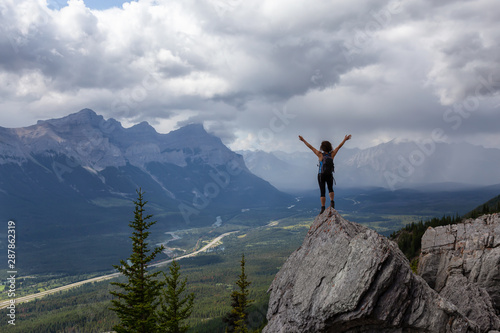 Adventurous Caucasian Girl with open arms is on top of rocky mountain during a cloudy and rainy day. Taken from Mt Lady MacDonald, Canmore, Alberta, Canada. © edb3_16