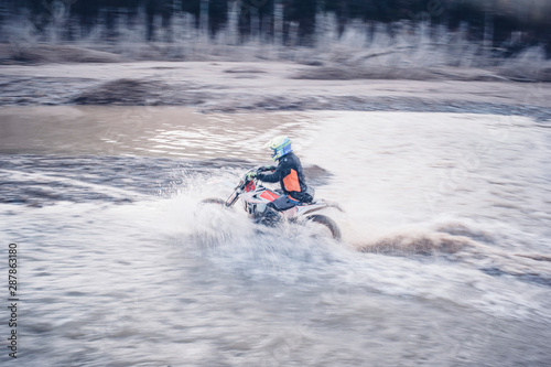 Motocross rider running in a large cloud of water inside the river