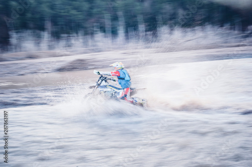 Motocross rider running in a large cloud of water inside the river