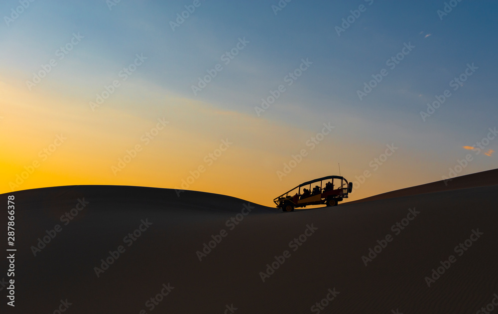  The silhouette of a sand dune and buggy in the Peruvian desert of Ica near the Huacachina Lagoon at sunset in Peru. 