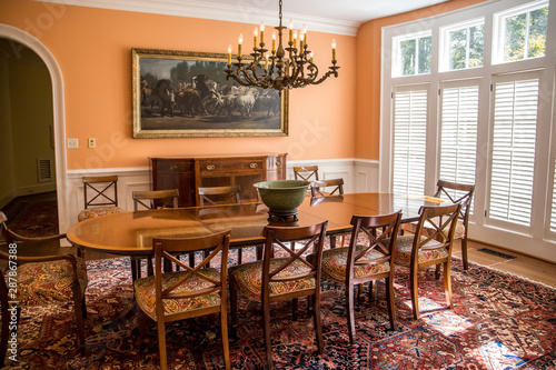 Orange peach colorful dining room with oriental rug and classic wood chairs and table with chandelier and artwork.