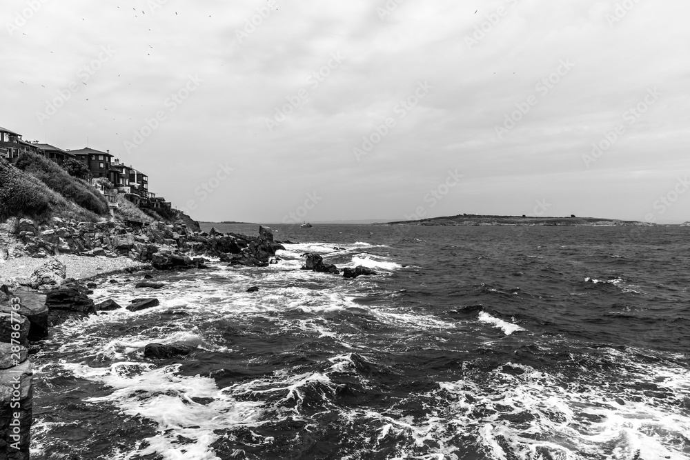 Obraz premium The rocky coast of the Black Sea near the ancient city of Sozopol. Bulgaria. In the In the background are the islands of St. Peter and St. Ivan. Black and white.