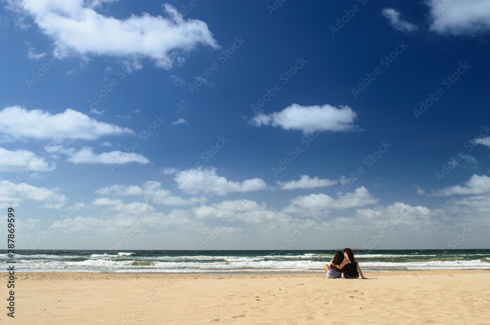 Horizonte de mar con mujeres abrazadas en la playa en día soleado con cielo azul y nubes Horizonte de mar con mujeres abrazadas en la playa en día soleado con cielo azul y nubes
