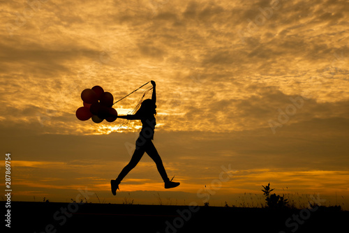 Freedom hand, Release and Let it go concept. Silhouette of a woman jumping with balloons with sunset backgroundThailand. Birthday balloon Holding by Happy Beautiful women in summer carnival photo