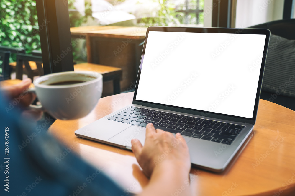 Mockup image of a hand using and touching on laptop touchpad with blank white desktop screen while drinking coffee Mockup image of a hand using and touching on laptop touchpad with blank white desktop screen while drinking coffee
