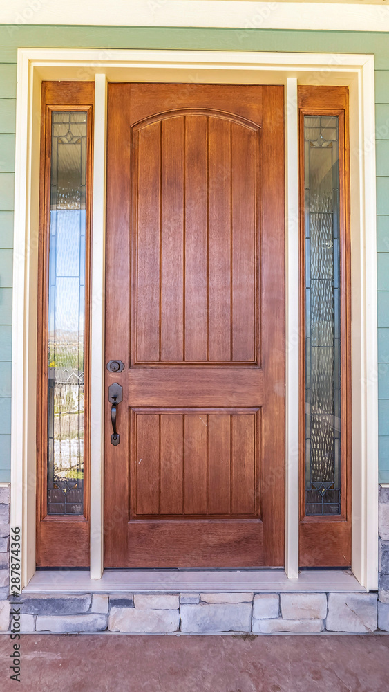 Vertical frame Front view of a home with green wall and brown wood door flanked by sidelights Vertical frame Front view of a home with green wall and brown wood door flanked by sidelights