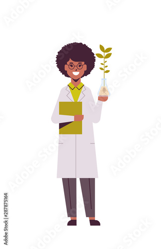 female scientist examining plant sample in test tube african american woman with clipboard in uniform making experiment in genetic lab research science chemical concept vertical full length flat