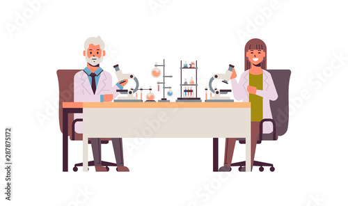 scientists couple using microscope man woman in uniform sitting at table making scientific experiments in chemistry laboratory with test tubes research science concept full length