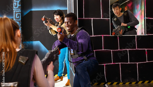Modern people of different nationalities with laser pistols playing laser tag on dark labyrinth © JackF