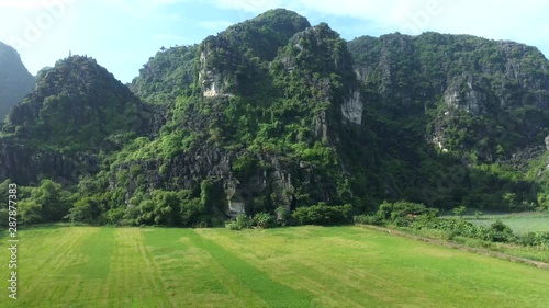 Aerial drone footage flying over rice fields and approaching limestone mountain of Tam Coc a famous Unesco world heritage in north Vietnam photo