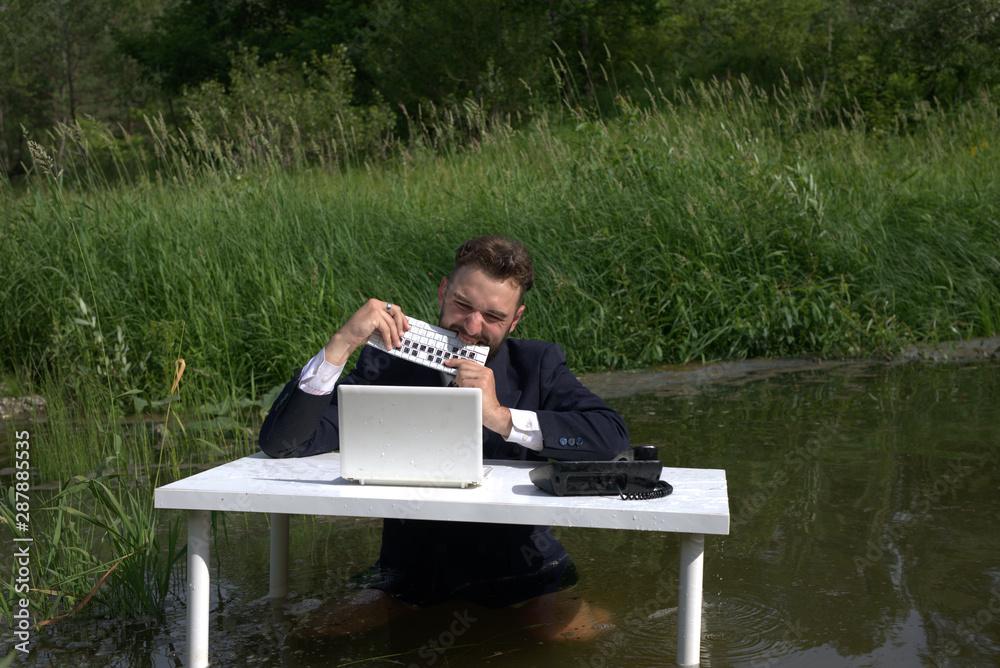 Fototapeta premium The young man is angry and bites the keyboard. Gnaws at the keyboard. nervous, tense situation in the workplace