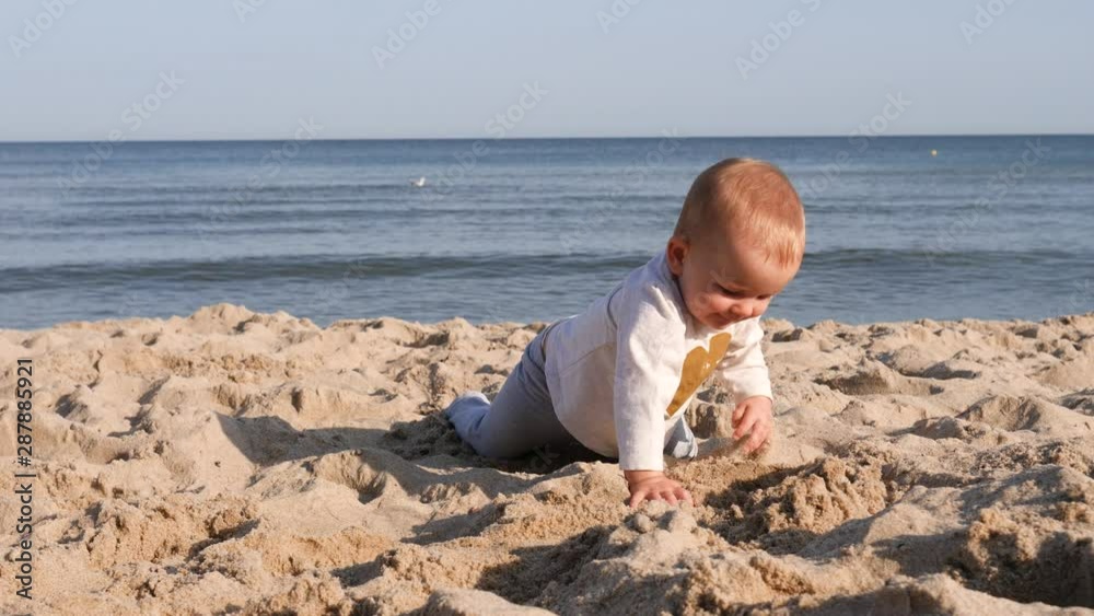 Toddler baby child play on beach sand crawl towards camera against Baltic sea background Toddler baby child play on beach sand crawl towards camera against Baltic sea background