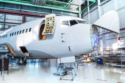 White passenger airplane under maintenance in the hangar. Checking mechanical systems for flight operations. The aircraft has opened weather radar