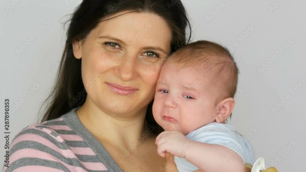 Young beautiful mother with long dark hair is holding a newborn infant baby of two months on a white background in studio Young beautiful mother with long dark hair is holding a newborn infant baby of two months on a white background in studio