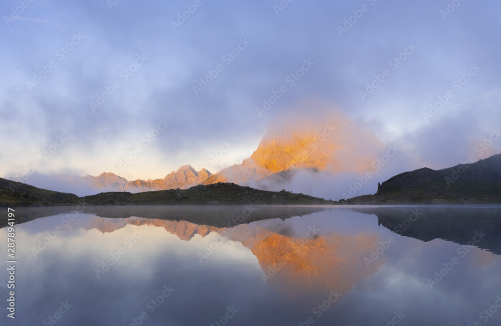 The Midi d'Ossau mountain between clouds is reflected in the gentau lake, Ayous Lakes, Pyrenees of France
