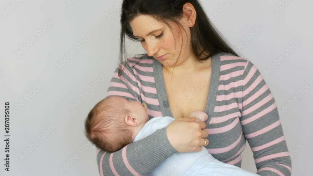 Young beautiful mother with long dark hair is holding a newborn infant baby of two months on a white background in studio Young beautiful mother with long dark hair is holding a newborn infant baby of two months on a white background in studio