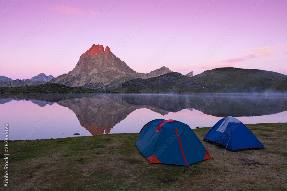 Tents next to the lake of Gentau, Ayous, and the Pico de Midi d'Ossau is reflected in its waters, Pyrenees, France.