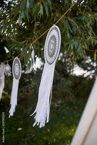 Boho style, wedding decoration. Ease and simplicity.Dream catcher white color, knit. Some pieces. Hanging outdoors in front of the tree. photo