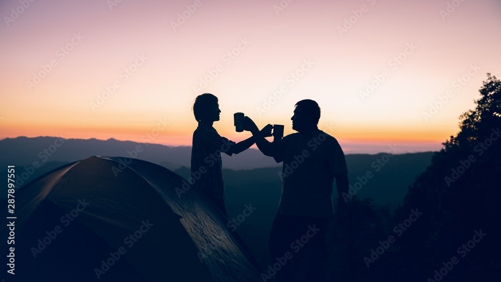 Happy two hiker man holding coffee cup near camping tent on mountains at sunset background. travel concept.