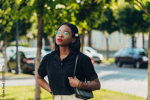 Young cool black skin girl with glasses walking in the street.