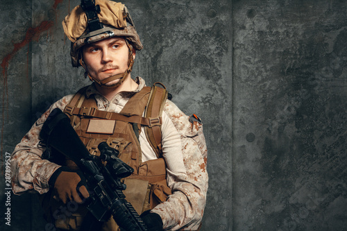 fully equipped army soldier in camo uniform and helmet, armed with pistol and assault service rifle