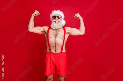 Portrait of nice attractive content cheerful funky glad content strong powerful cool gray-haired strong man trainer instructor bodybuilder showing muscles isolated on bright vivid shine red background