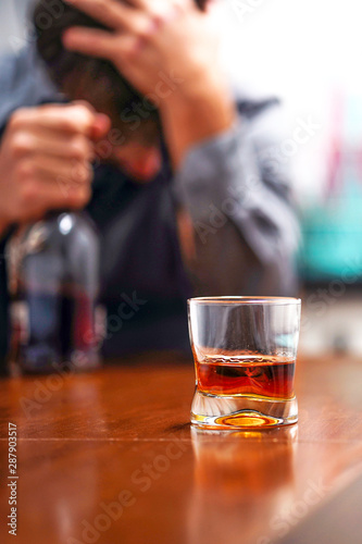  A glass of whiskey on the table on the background of a drunken man. Alcoholic father 