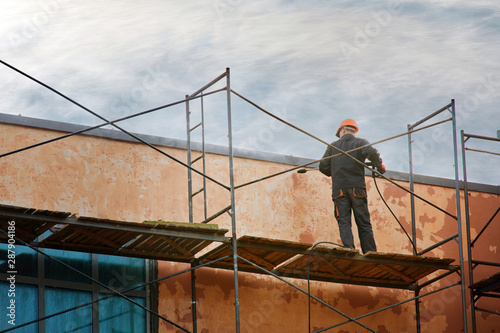 Wallpaper Mural Worker in uniform cleans wall facade with pressure washer while standing on scaffolding. High pressure water cleaner. Professional facade cleaning services washing building facade with pressure water Torontodigital.ca