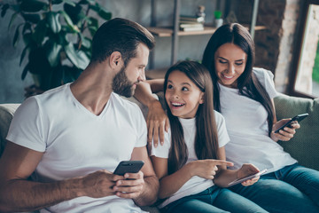Portrait of nice attractive lovely cheerful cheery friendly family mommy daddy wearing casual white t-shirts jeans denim sitting on sofa using 5g app at industrial style interior living-room