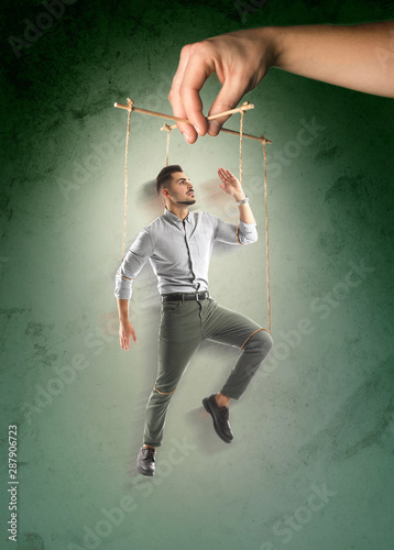 Foto Hand of puppeteer manipulating man as marionette on color background