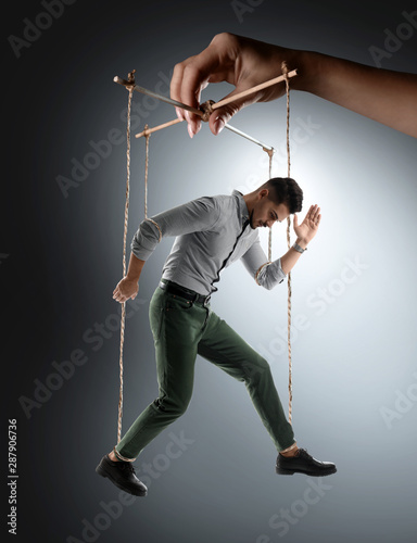 Obraz na plátně Hand of puppeteer manipulating man as marionette on grey background