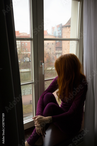girl sitting on a windowsill and looking at the evening city