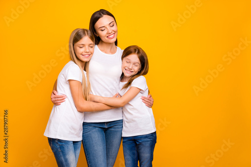 Two small ladies hugging young and beautiful babysitter wear casual white t-shirts isolated yellow background © deagreez