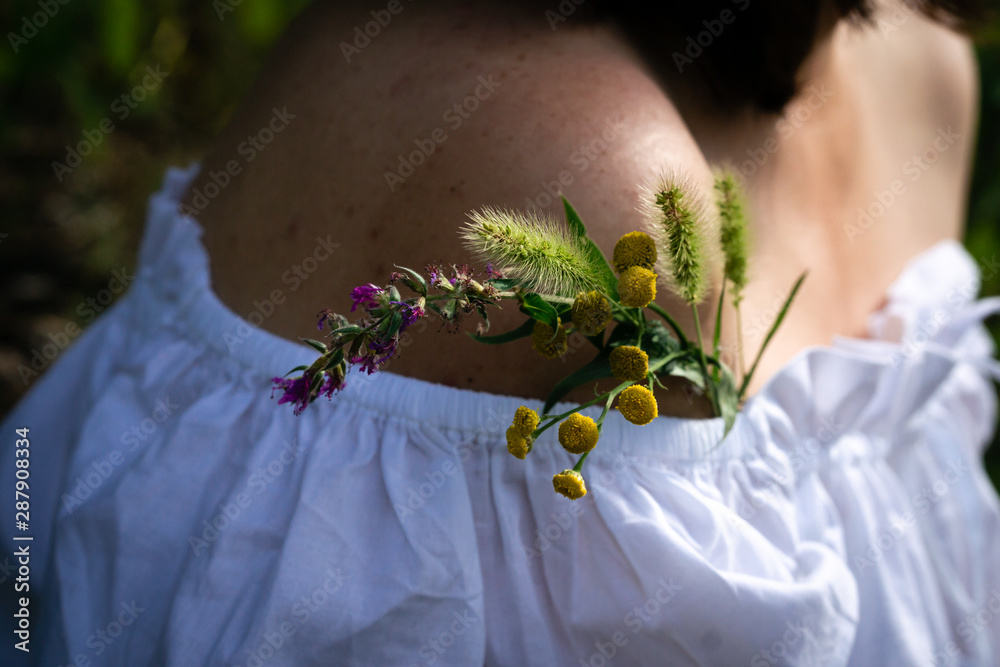 Obraz premium A small bouquet of meadow yellow and purple pink flowers in a white dress on a bare shoulder. Warm tone. Horizontal orientation.