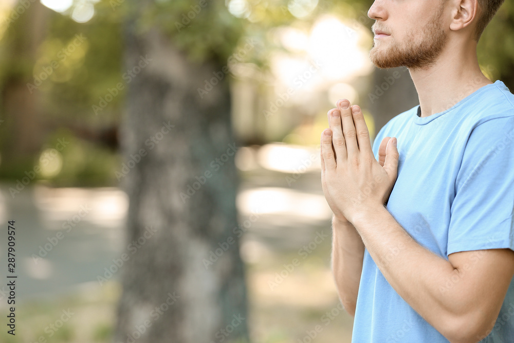 Religious young man praying to God outdoors Religious young man praying to God outdoors