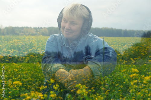 Happy smiling mature woman sitting wearing headphones and listen to relaxation music on field with alot of yellow flowers. Double exposure. Sonic Therapy. Sensivity to nature. photo