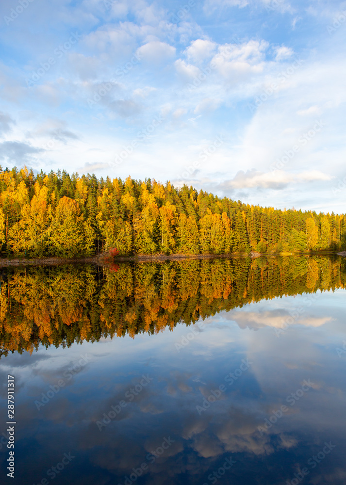 Amazing colors in the nature during sunny autumn day in Finland. Colorful forest and reflection in the calm water.