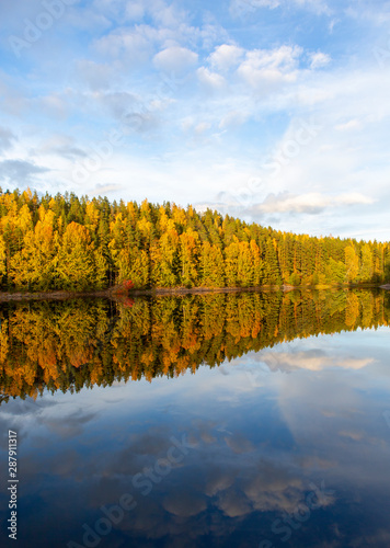 Amazing colors in the nature during sunny autumn day in Finland. Colorful forest and reflection in the calm water.