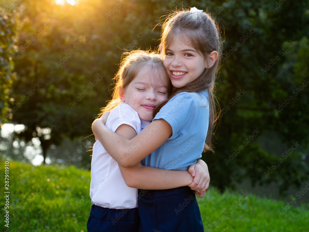 Fototapeta premium Two little girls friends in school uniform hug each other in the park.