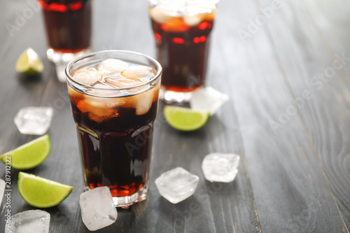 Glasses of cold cola, ice cubes and lime on wooden table