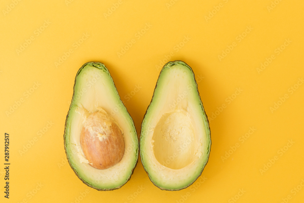 High angle view of avocado cut in half on yellow background (selective focus)
