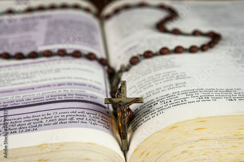 Closeup open holy bible and beautiful Christian rosary beads on top main focus at Jesus Christ crucifix.