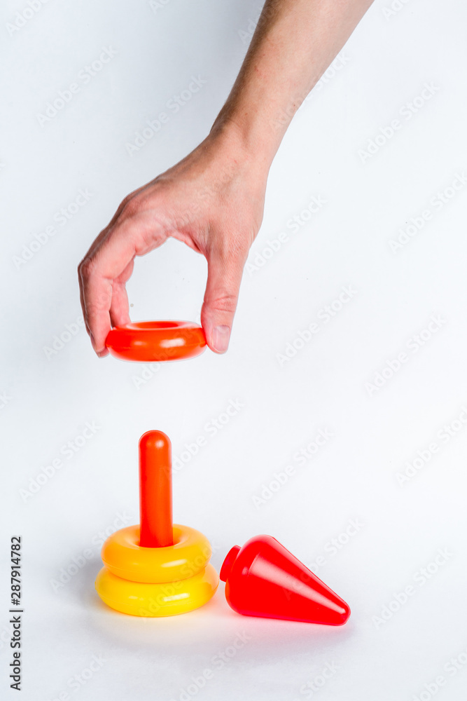 Construction of a colored children's pyramid on a white isolated background.. A woman's hand makes the final touch. Easy, simple and fast solution of a complex problem. Copy space Construction of a colored children's pyramid on a white isolated background.. A woman's hand makes the final touch. Easy, simple and fast solution of a complex problem. Copy space