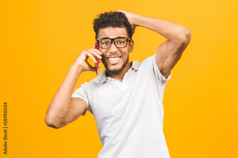 Happy winner. Portrait of a cheerful african american guy talking on mobile phone isolated against yellow background. Happy winner. Portrait of a cheerful african american guy talking on mobile phone isolated against yellow background.