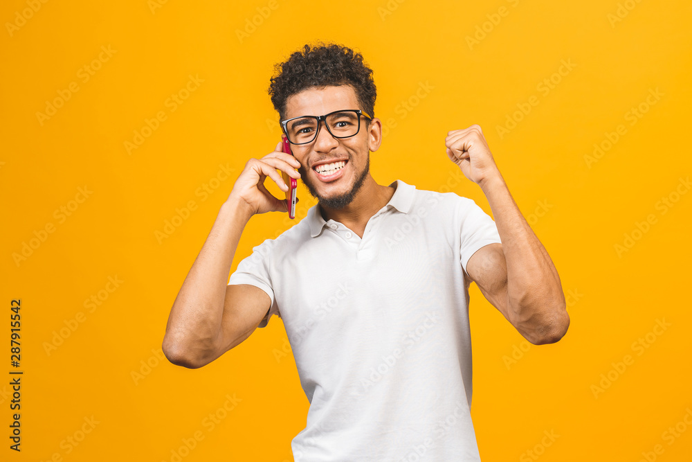Happy winner. Portrait of a cheerful african american guy talking on mobile phone isolated against yellow background. Happy winner. Portrait of a cheerful african american guy talking on mobile phone isolated against yellow background.