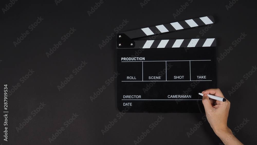 Black Clapperboard or clap board or movie slate with right hand holding pen use in video production ,film, cinema industry on black background.